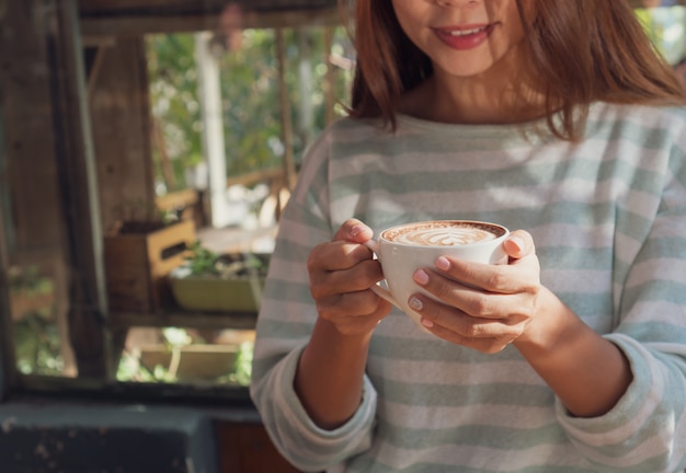 Female hand holding cup of hot cocoa or chocolate on wooden table, close up