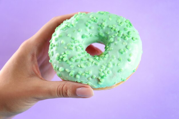 Female hand holding delicious donut on color background closeup