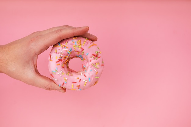 Female hand holding delicious donut on pink background