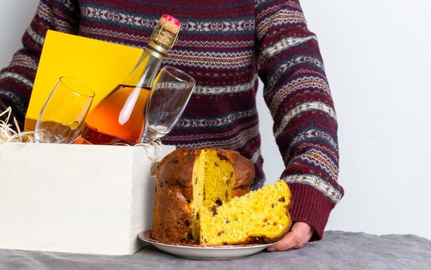 Mano femminile che tiene il pezzo italiano del panetone di pasqua vicino alla scatola di consegna con la bottiglia di champagne.