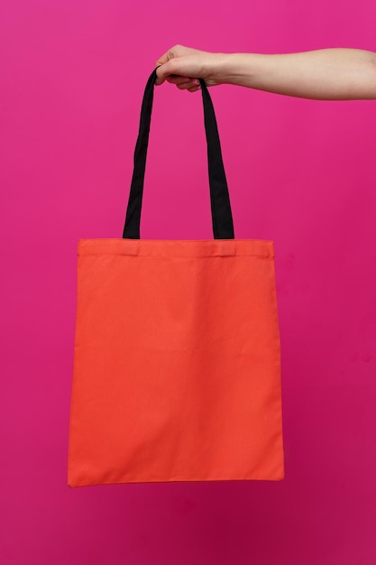 Female hand holding eco or reusable shopping bag against pink
background