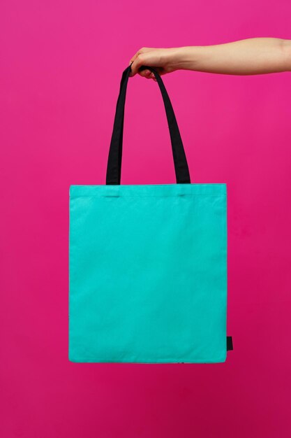 Female hand holding eco or reusable shopping bag against pink\
background