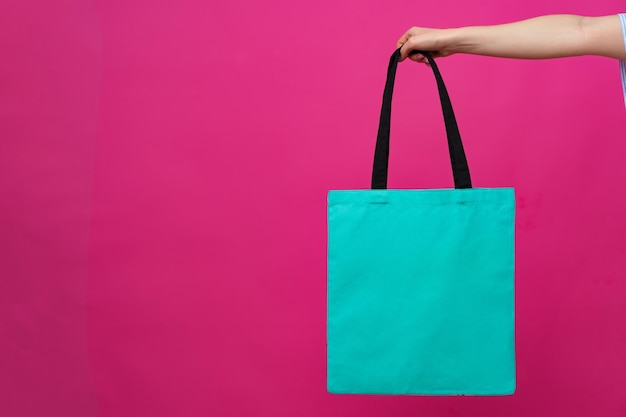 Female hand holding eco or reusable shopping bag against pink background