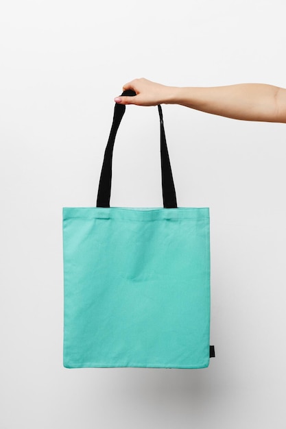 Female hand holding eco or reusable shopping bag against white background