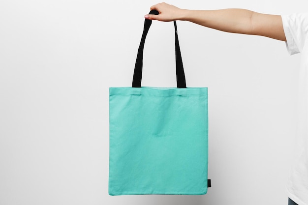 Female hand holding eco or reusable shopping bag against white\
background