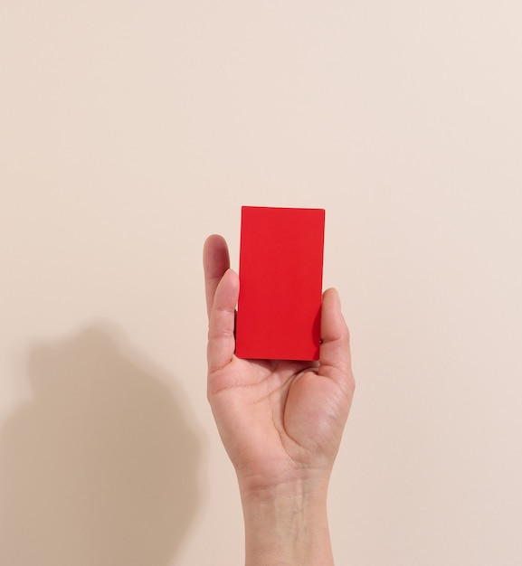 Женская рука держит пустую красную бумагу на бежевом фоне. Скопируйте и вставьте изображение или текст, крупный план