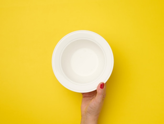 Female hand holding an empty round plate on a  yellow background, top view