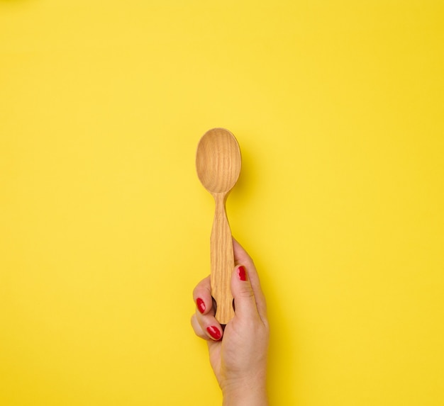 Female hand holding empty wooden spoon on yellow background