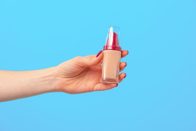 Female hand holding facial foundation against blue close up