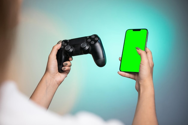 Mano femminile che tiene un controller di gioco e uno schermo verde del telefono cellulare su sfondo colorato.