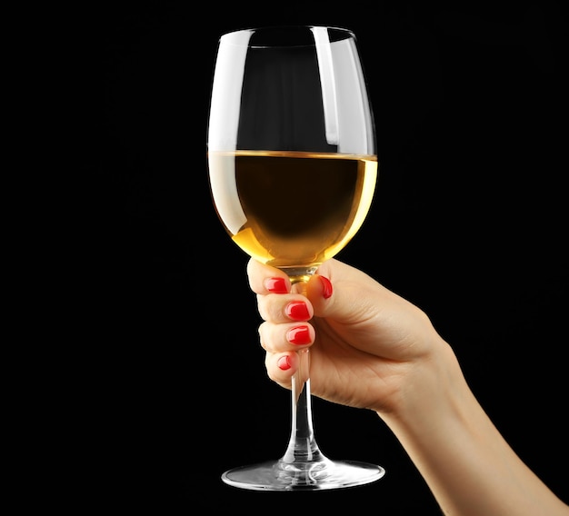 Female hand holding glass of wine on black background