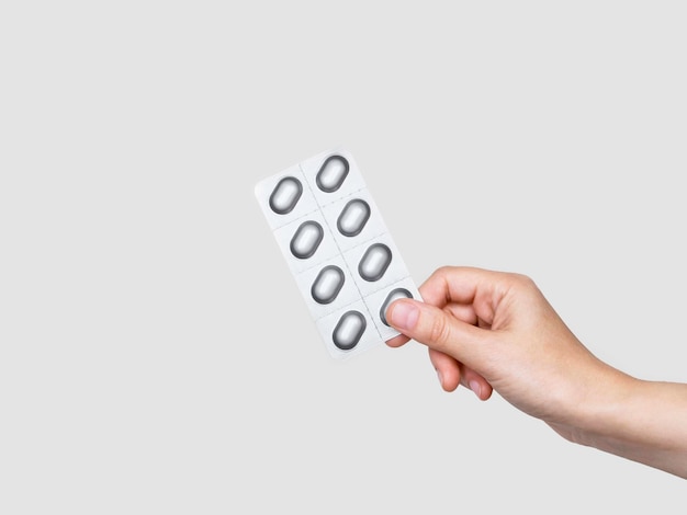 female hand holding gray blister with pills on gray background