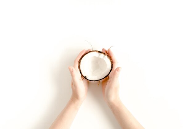 Female hand holding half coconut on white background flat lay top view