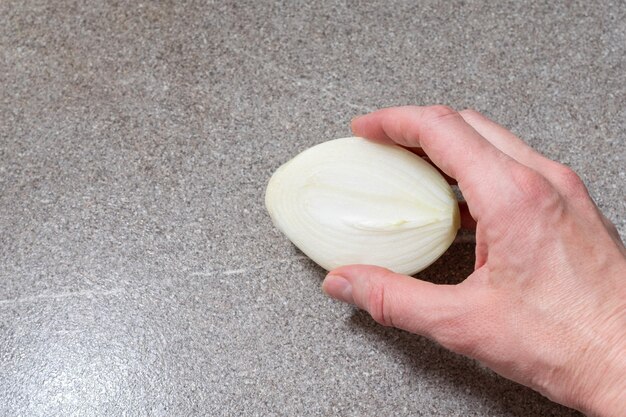 Female hand holding half of raw onion on gray trending background copy space top view Homemade food