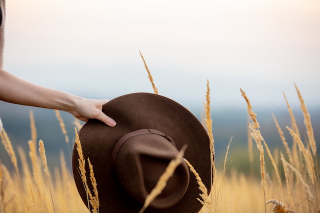 田舎で黄色い草の上の帽子を持っている女性の手