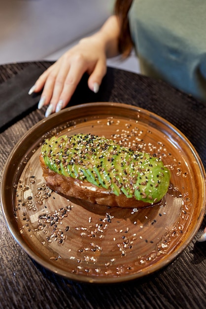 Female hand holding healthy avocado toast ripe hass avocado wholegrain bread sesame flax seeds vegan