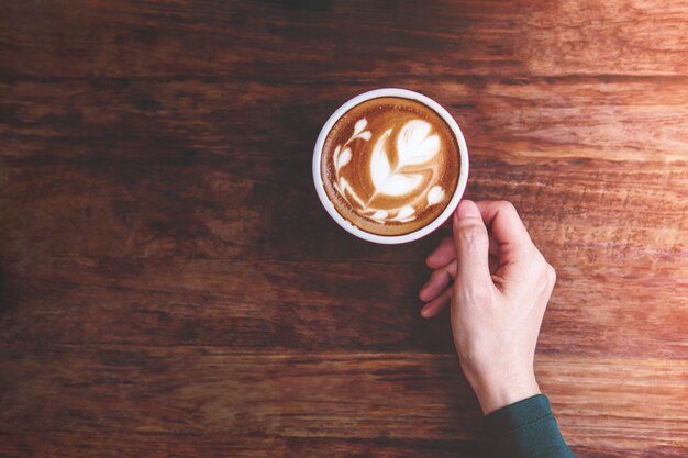 Female hand holding a Hot Latte Coffee Cup on the wooden 