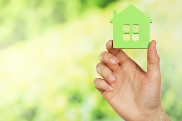 Female hand holding house on green blurred background