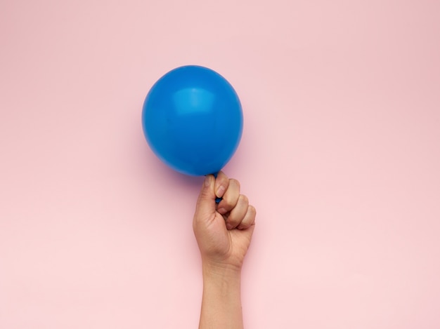 Photo female hand holding an inflated blue air balloon on a pink background, close up