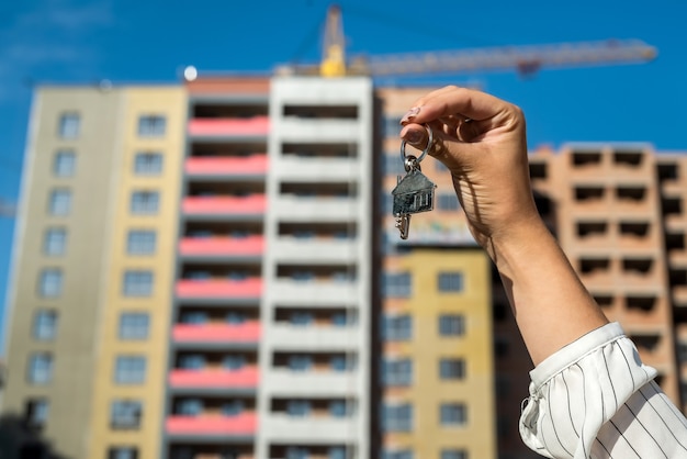 Female hand holding keys in front of a new home. sale concept