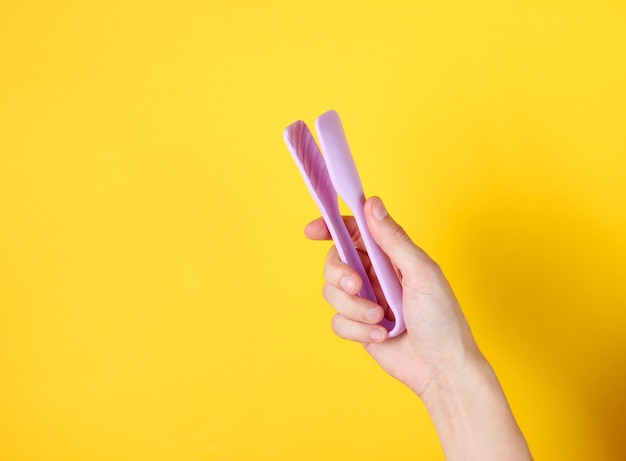 Female hand holding kitchen tweezers on yellow.