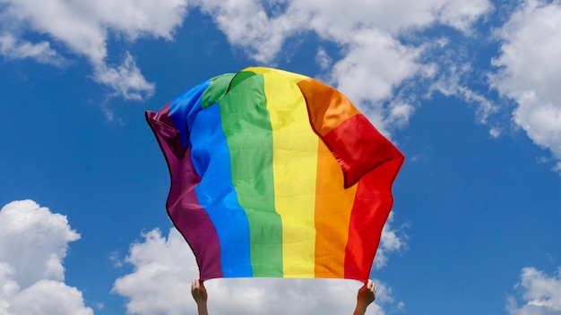 Female hand holding a LGBT gender identity flag on a background of blue cloudy sky on a sunny windy summer day during the celebration of the month of dignity at the parade