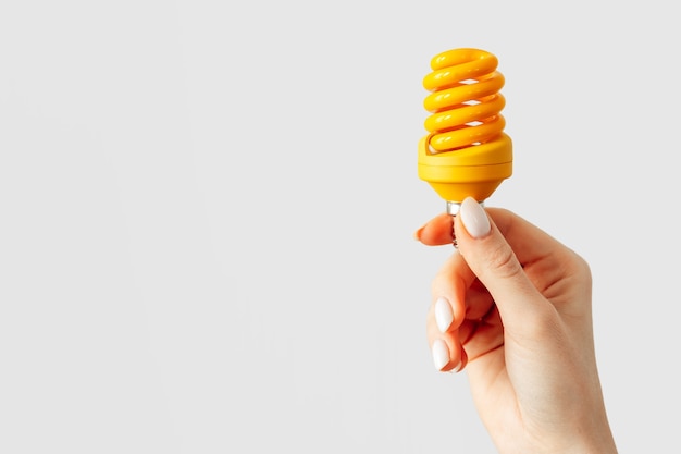 Female hand holding light bulb against gray background