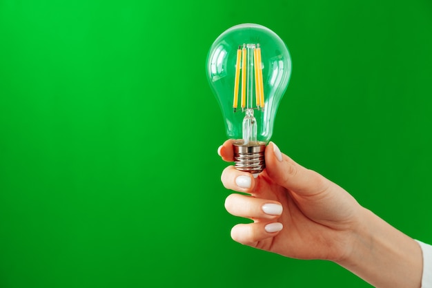 Female hand holding light bulb against green background