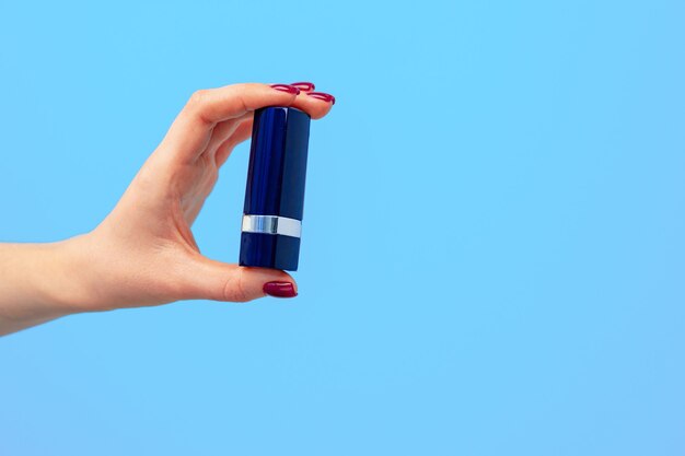 Female hand holding lipstick against blue background close up