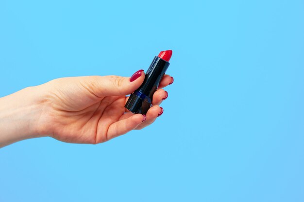 Female hand holding lipstick against blue