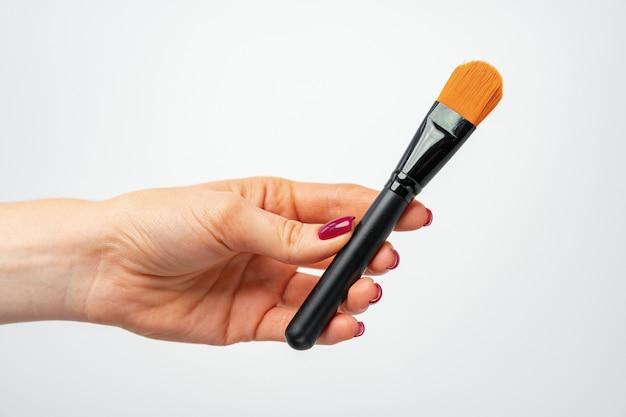 Female hand holding make up brush against gray background close up