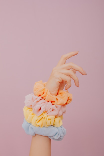 Female hand holding many scrunchies . Female hand isolated on pink surface