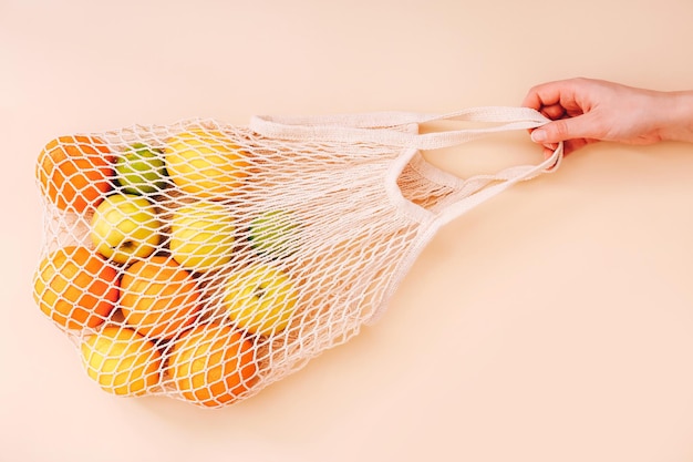 Female hand holding mesh eco bag with fruits on light background. Healthy clean eating. Eco shopping concept.