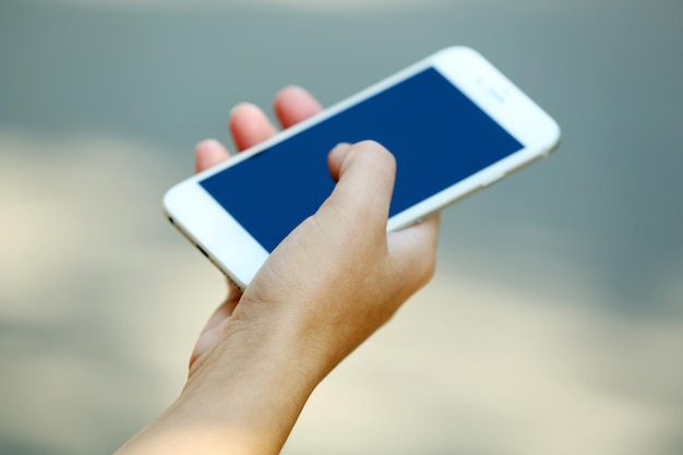 A female hand holding a mobile phone outdoors on blurred background