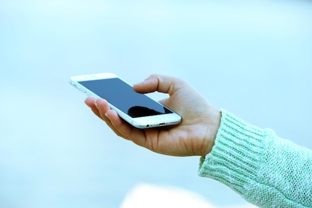 A female hand holding a mobile phone outdoors on blurred background