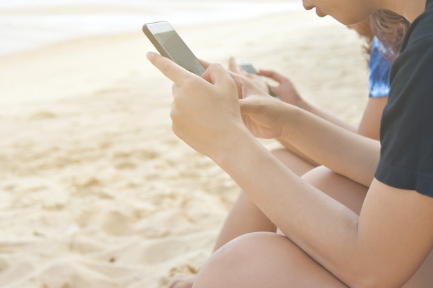 Female hand holding modern smartphone on seaside beach