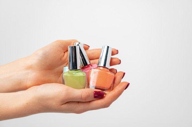 Female hand holding nail polish against white background close up