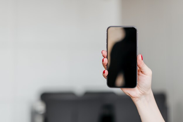 Female hand holding a new phone with copy space blank empty screen at home in the apartment