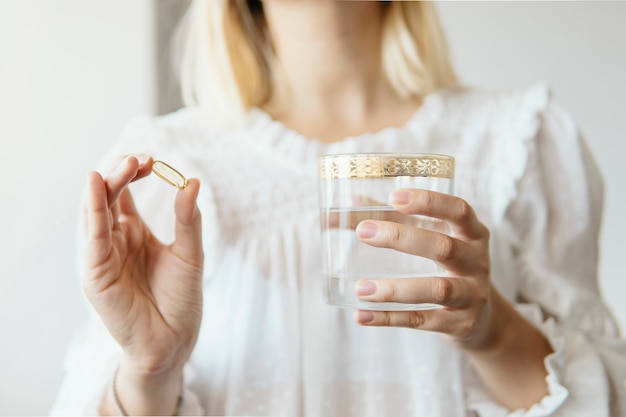 Female hand holding Omega 3 fish oil supplement capsule and glass of water