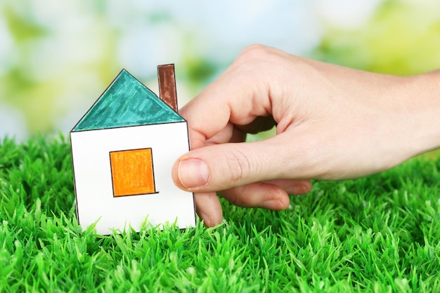 Female hand holding paper house on green background close up