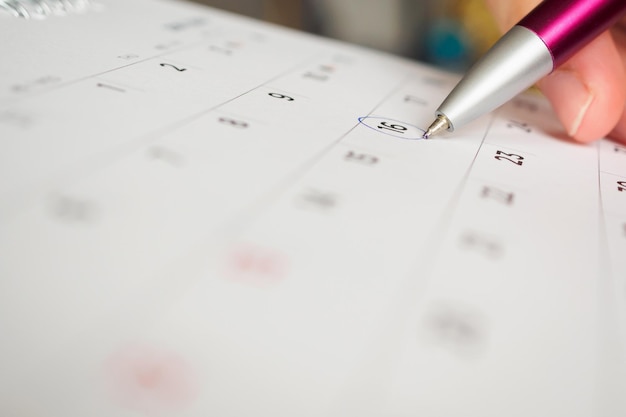 Female hand holding pen circle mark on calendar page