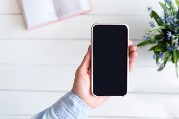 Female hand holding a phone on light background. Black blank screen.