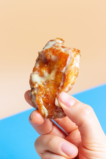 Female hand holding a piece of fried chicken on a blue and brown background close-up.