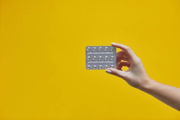 Female hand holding pills in blister on yellow