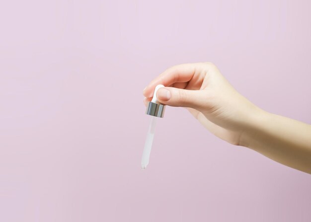 female hand holding a pipette with serum on a pink background skin care concept