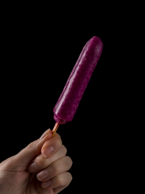 Female Hand Holding a Popsicle on black background. Grapes.