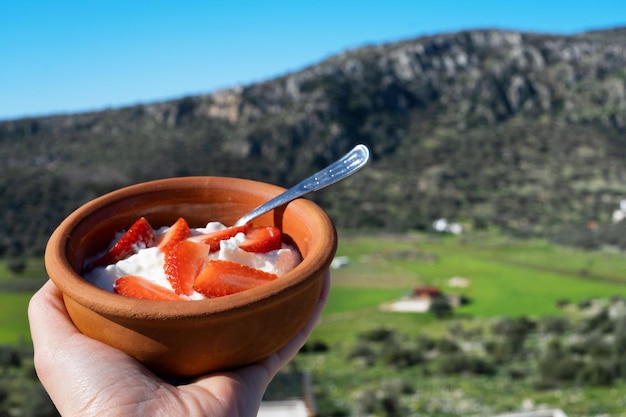 Female hand holding pot with strawberry yoghurttraditional turkishgreek food on background of beautiful valleymountainsHaving healthy lunchquick meal with breathtaking landscape view