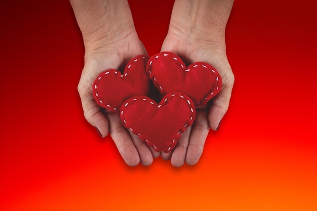 Female hand holding red hearts on red background