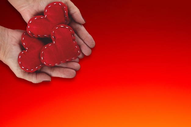 Female hand holding red hearts on red background