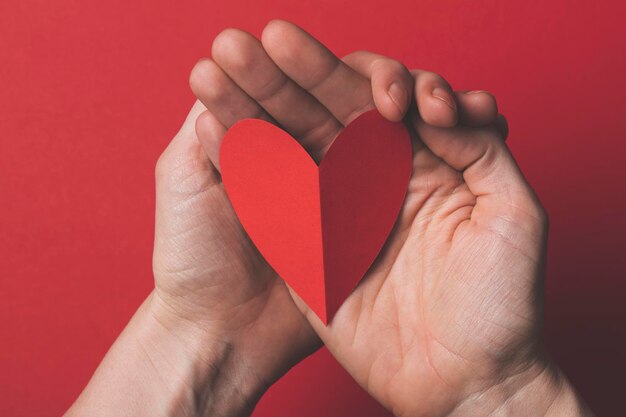 Female hand holding a red paper cut out heart on a plain red background